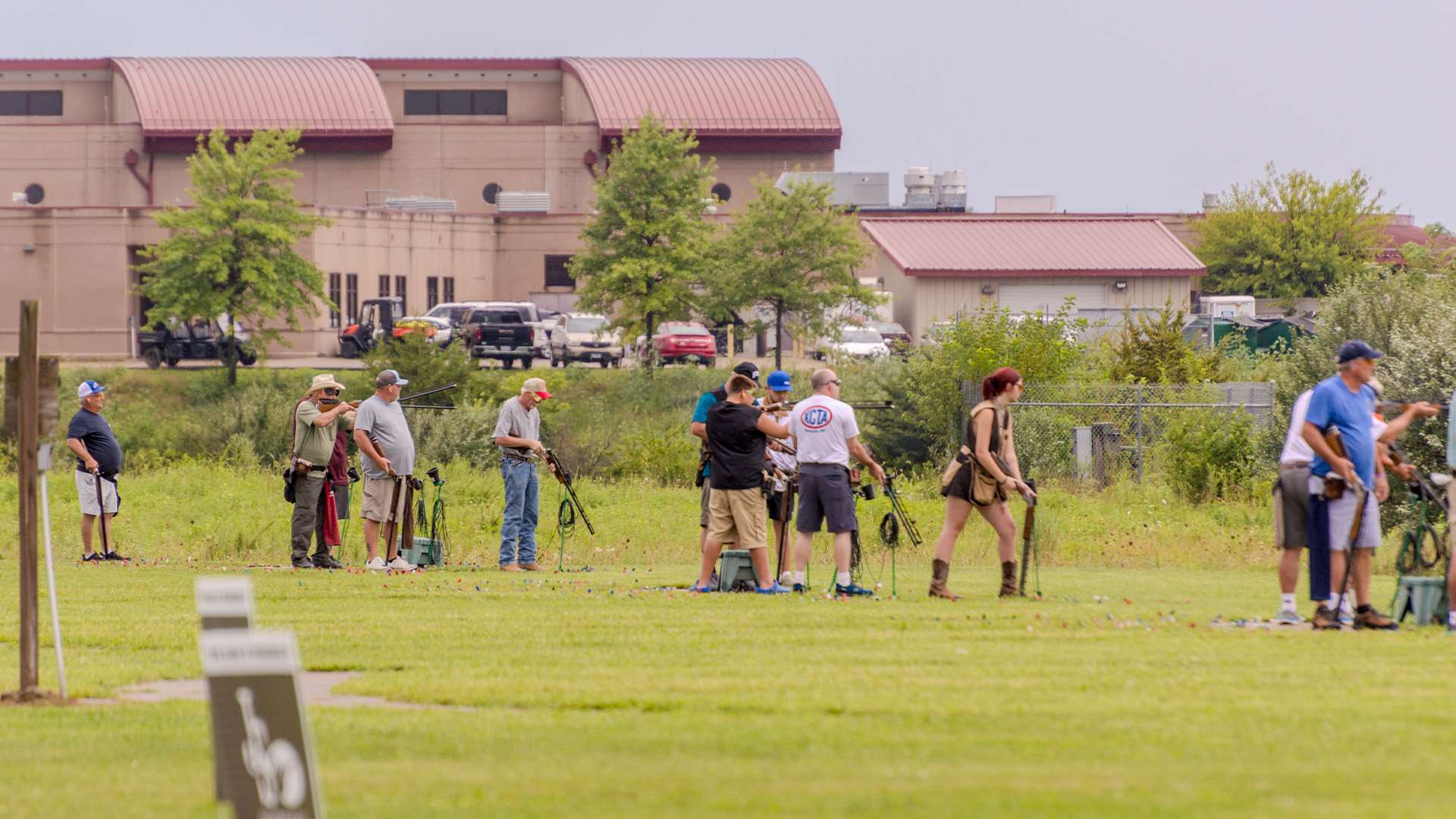 Trapshooters on the firing line at the Grand American with the World Shooting and Recreational Complex's main administration building and parking lot in the background.