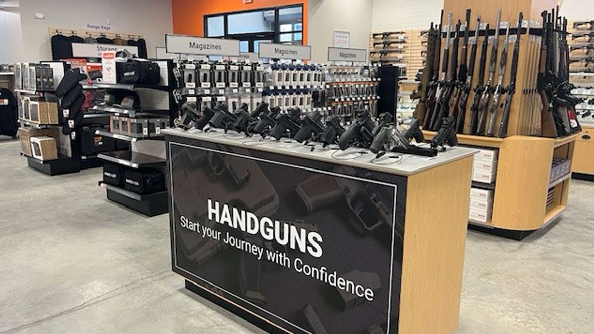 Range USA self-service handgun display case and long gun display tower stocked with shotguns and rifles at a Range USA store