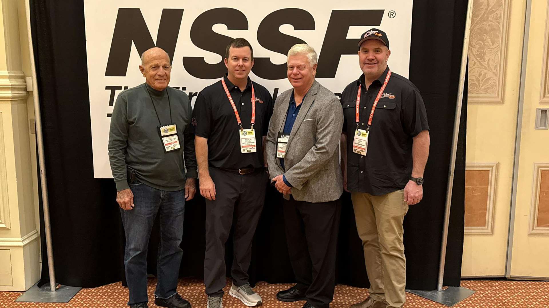 Four men pose in front of an NSSF backdrop at SHOT Show 2026 in Las Vegas including Lynn Gipson in a grey blazer with industry colleagues