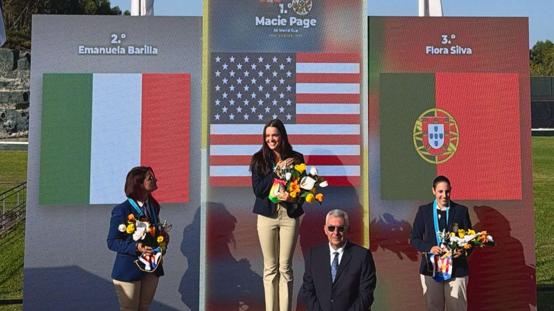 Macie Page stands atop the Ladies podium under a U.S. flag video board flanked by the Italian and Portuguese medalists