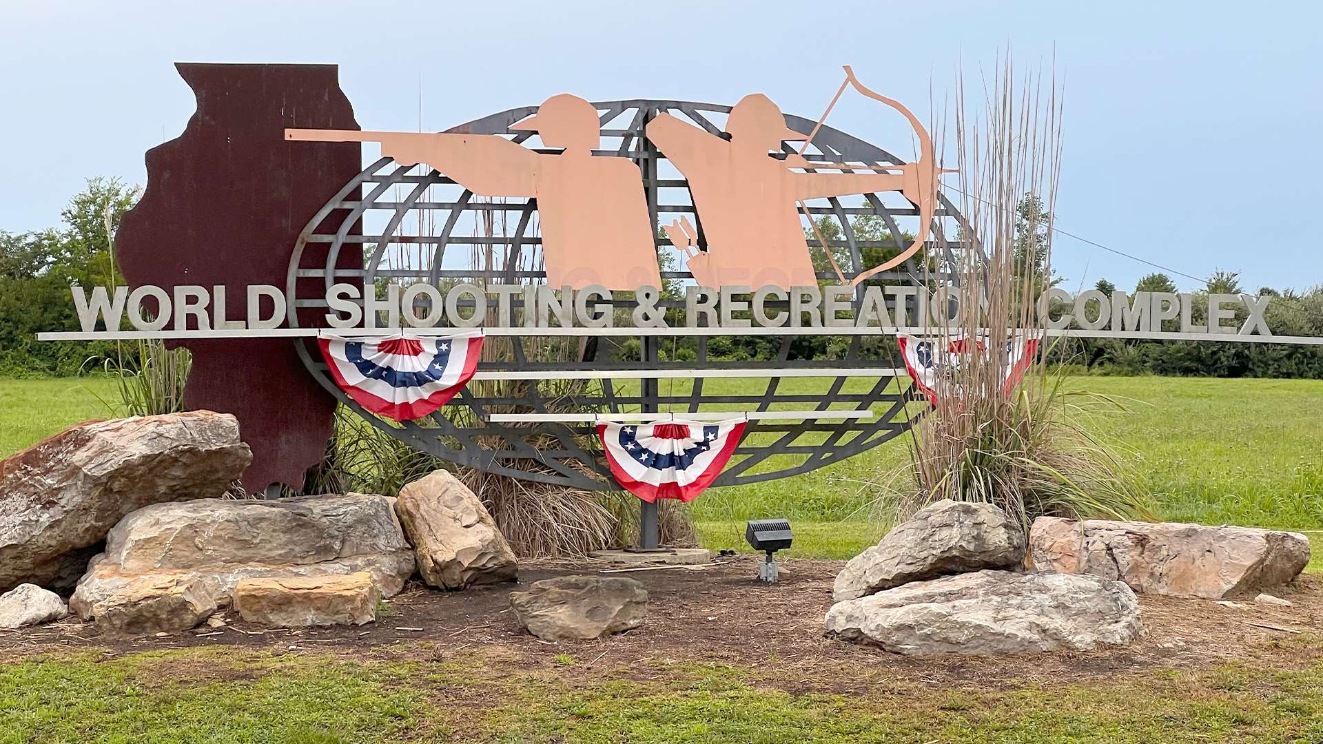 The World Shooting &amp; Recreational Complex entrance sign in Sparta, Illinois, featuring a steel globe and shooter silhouettes, decorated with patriotic bunting