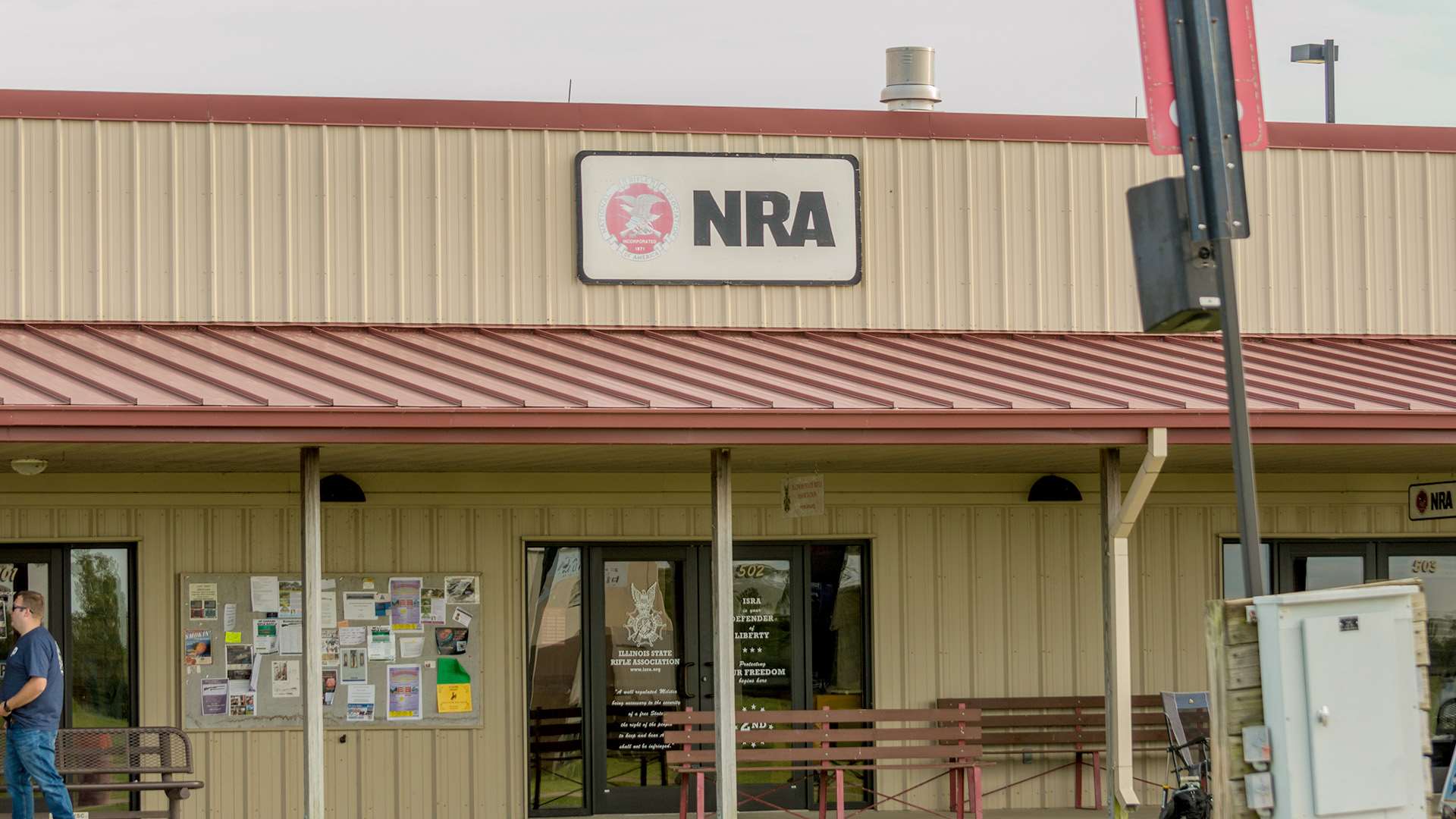 The NRA building on the vendor row at the World Shooting and Recreational Complex, its sign visible above a covered walkway lined with benches and a community bulletin board
