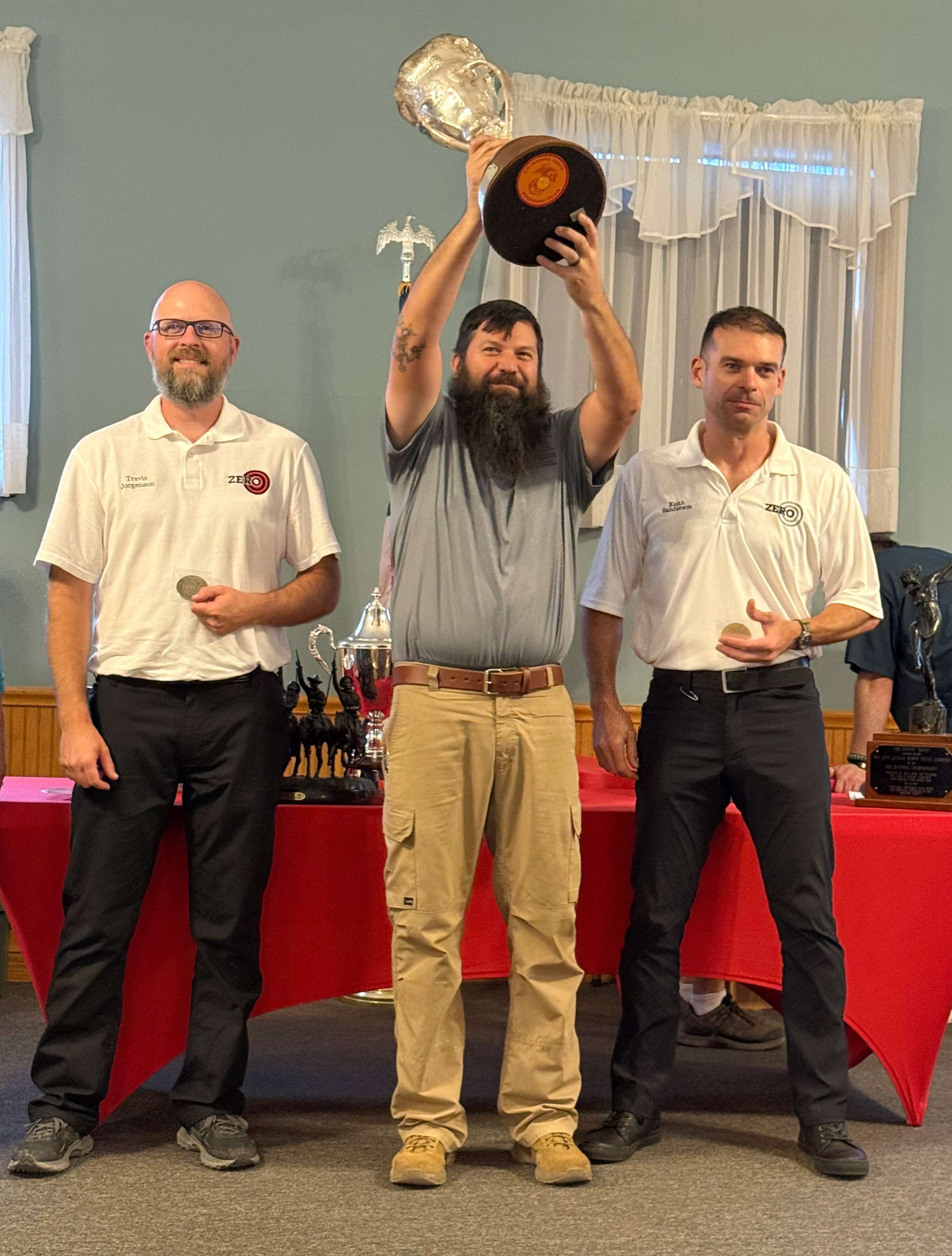 Jon Shue raises a silver trophy above his head while flanked by Travis Jorgenson and Keith Sanderson holding their medals at the awards ceremony