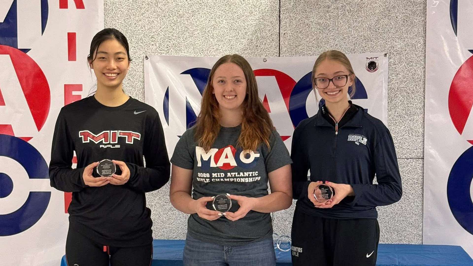 Three collegiate rifle athletes stand together on the podium at the 2026 Mid-Atlantic Rifle Conference Championship at MIT