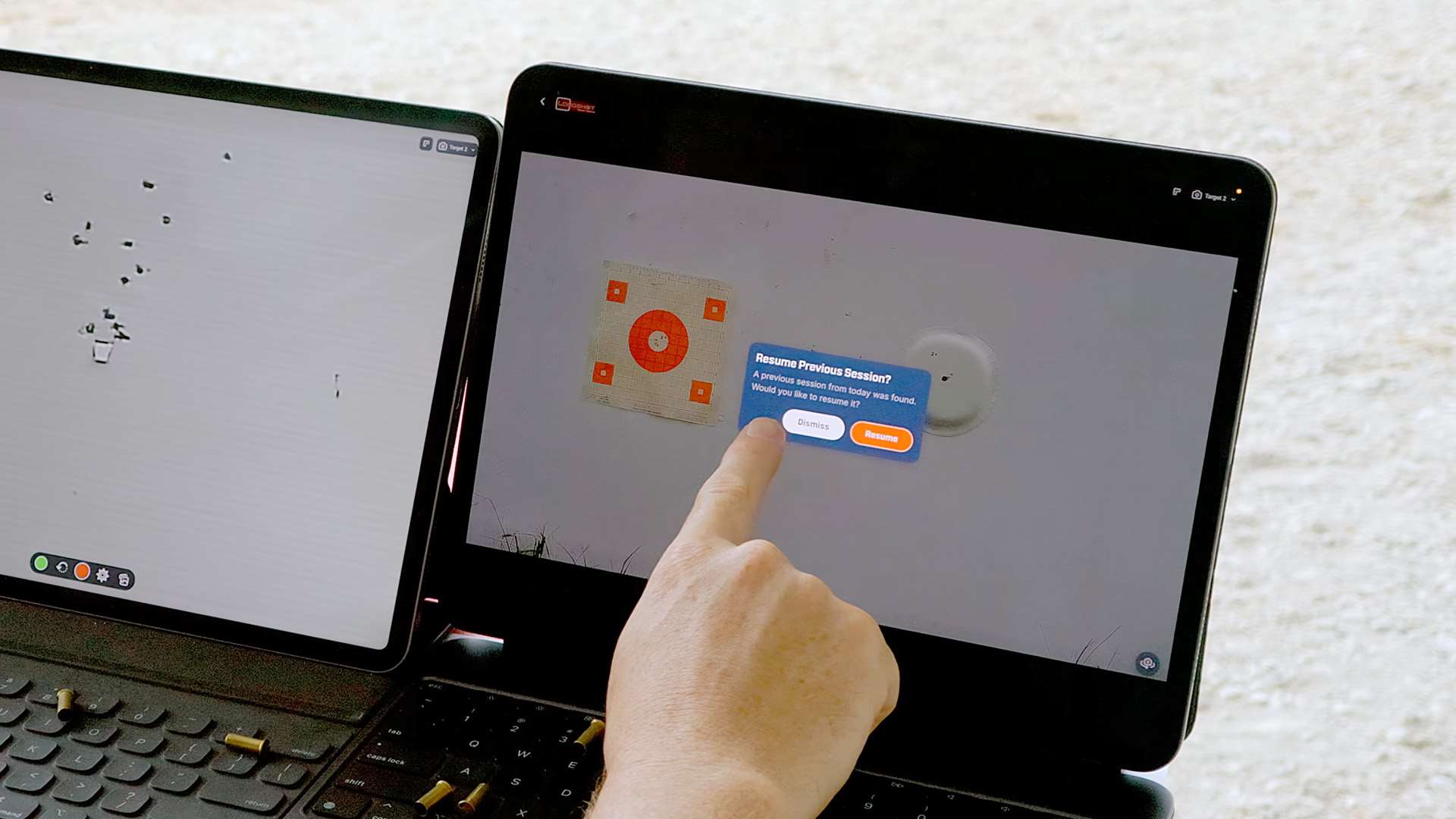 A finger hovers over a "Resume Previous Session?" prompt on a tablet showing a live camera view of an orange bullseye target downrange