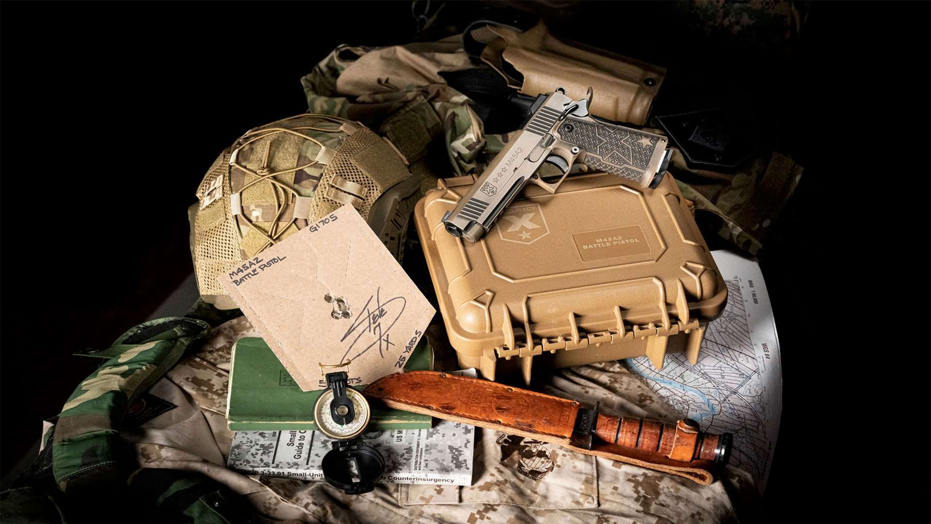 M45A2 Battle Pistol on a tan hard case with a signed test target, compass, fighting knife and map amid military gear