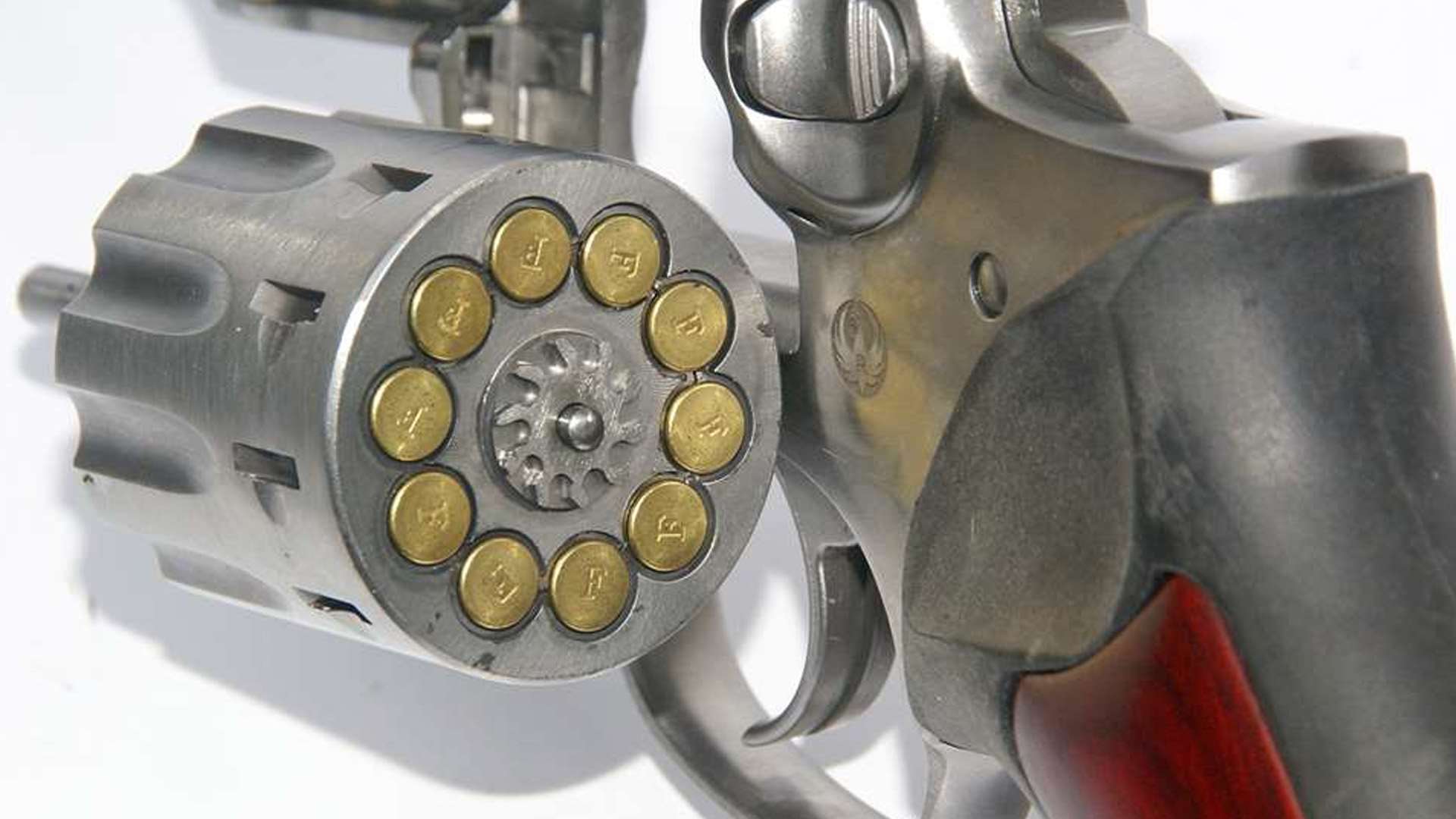 Close-up of a stainless Ruger GP100 revolver with its 10-shot cylinder swung open and loaded with .22 LR cartridges