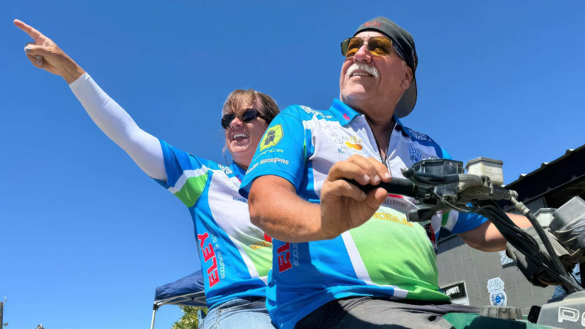 Kurt and Maria Grimes sit together on an ATV at the Area 2 range, both smiling broadly as Maria points toward the sky during the Area 2 match in 2024