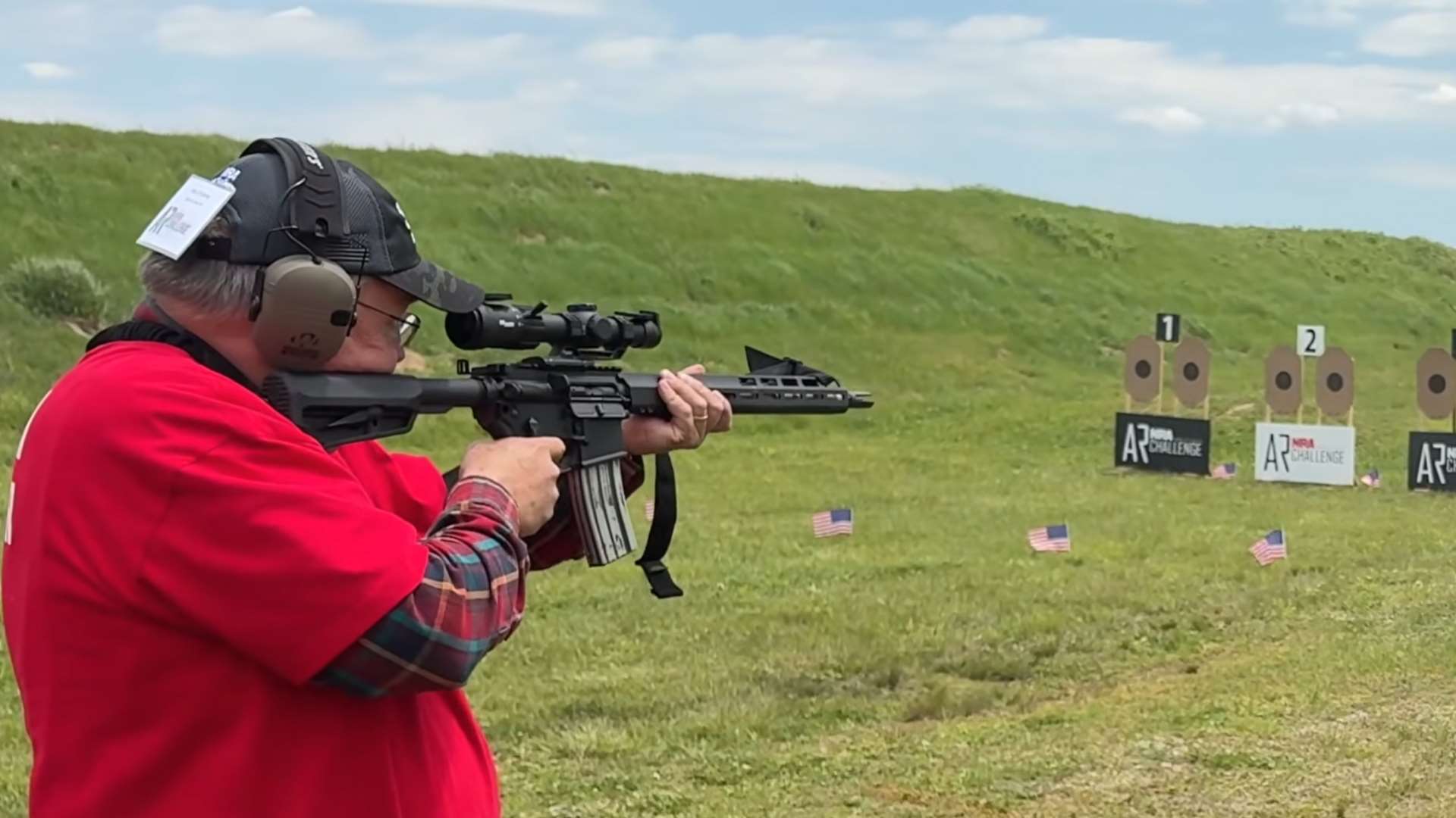 Match director in red shirt shooting AR-15 from standing position at NRA America’s Rifle Challenge targets during Level 1 live-fire exercises at Camp Atterbury Match Director Summit