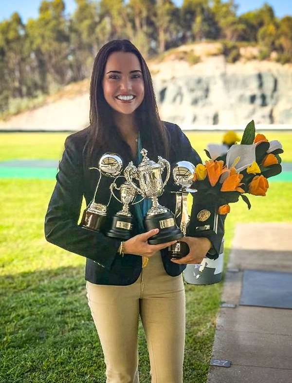 Vertical portrait of Macie Page in a navy competition blazer holding trophies at the Braga range