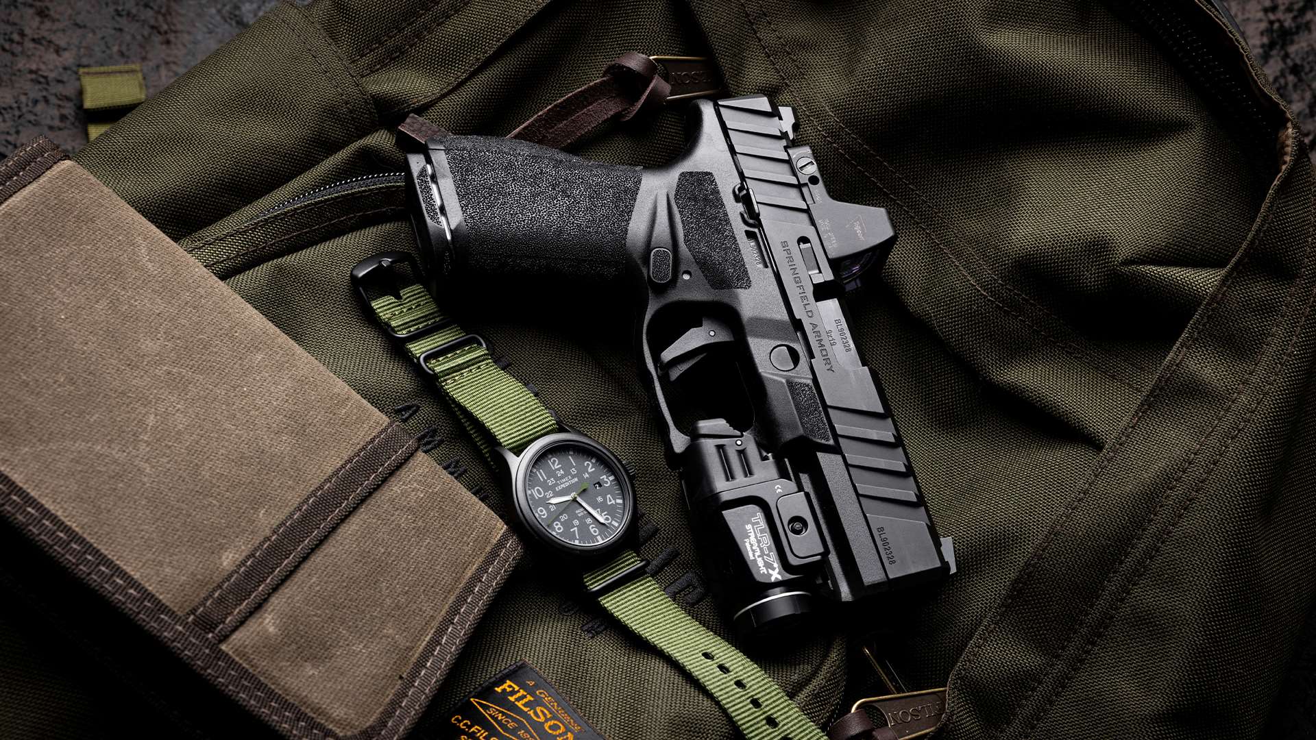 Springfield Armory Echelon Alpha 4.0C handgun fitted with a Streamlight TLR-7X light and red dot sight, photographed on an olive canvas Filson bag alongside a Timex Expedition field watch