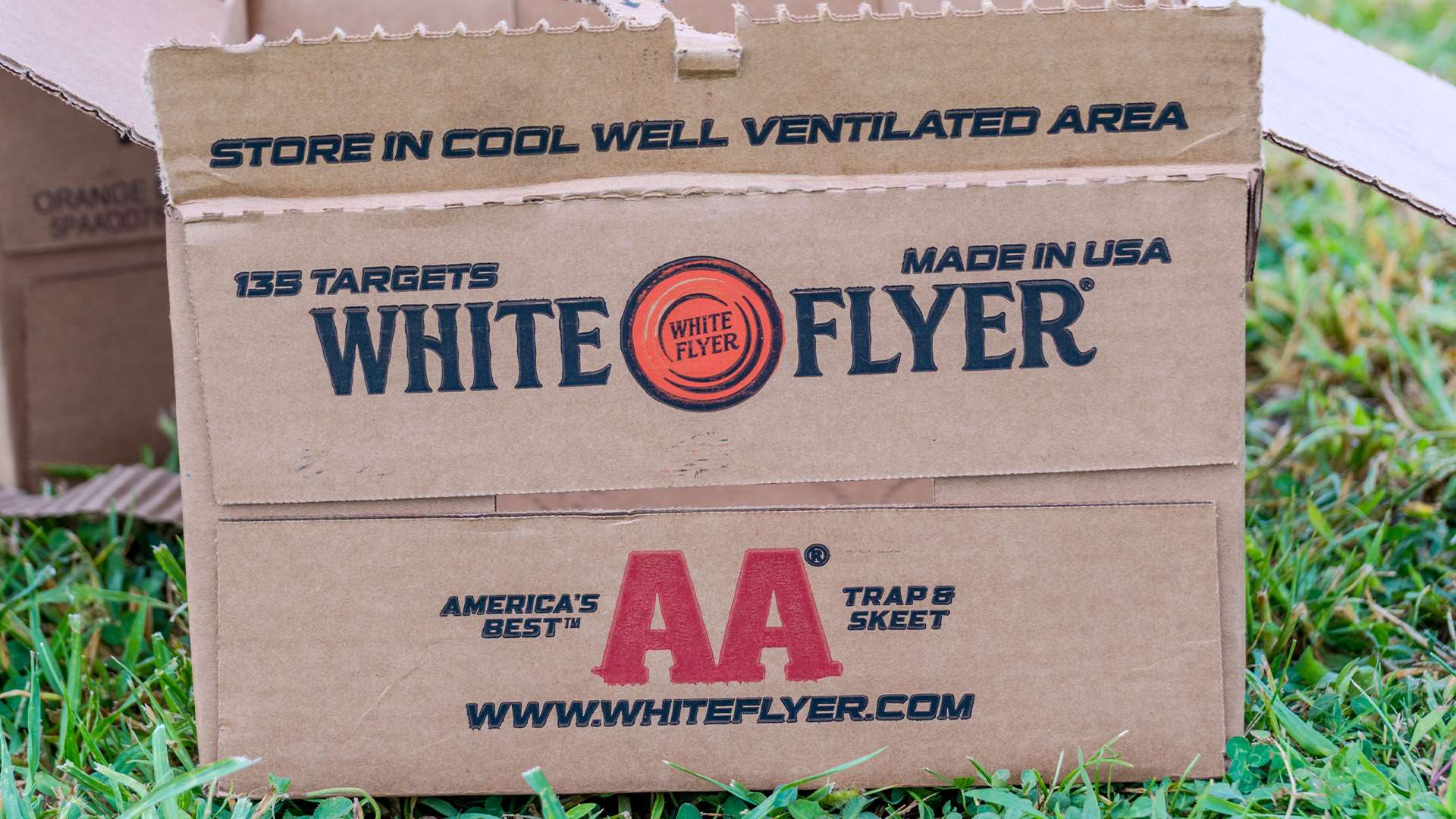 An open cardboard case of White Flyer AA trap and skeet targets sitting in the grass at the Grand American