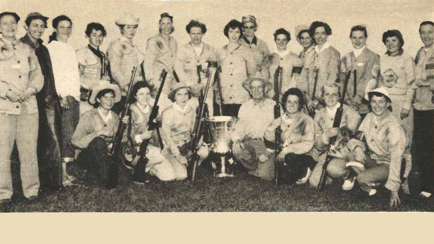 Thurman Randle (at right of trophy) and Randle Trophy Women&#x27;s International Postal Team. (I. to r., kneeling) Miss Dixie Lange, Miss Priscilla Haig, 1956 National Smallbore Women&#x27;s Champion Mrs. Viola E. Pollum, Miss Marjorie Firrantello, Miss Judy Mortenson, Mrs . Barbato Norton (coach); (standing) Mrs. Ruth Tohill (team coach), Miss Winnifred Carr (alternate ), Mrs. Pat Burkhalter (coach), Miss Roberta Gubbins, Miss Judy Regan (coach), Mrs. Ruth Morgan (coach), Mrs. Mary l. Greer, Miss Dorothy Morris, Mrs. Suzanne K. Johnson (coach}, Miss Barbara Winton, Mrs. Gwen H. Rossman (coach), Mrs. Lucille Wolford, Miss Kristin Stal (alternate), Mrs. Esther I. Smith (coach), Mrs. Marianne Jensen Driver (team captain)