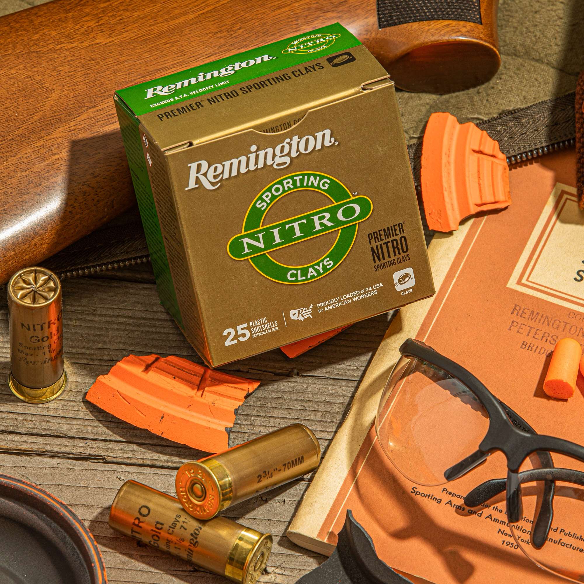 Overhead view of a Remington Premier Nitro Sporting Clays box with 12-gauge shells, clay target fragments, clear shooting glasses, foam earplugs and a vintage orange Remington-Peters publication