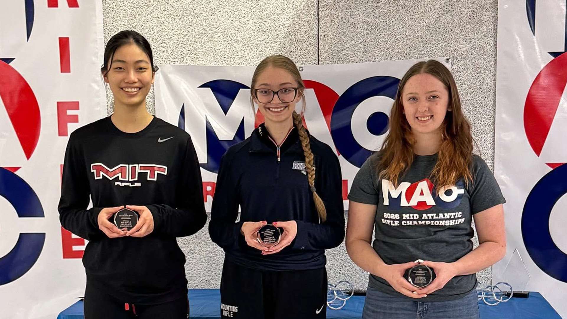 Three collegiate rifle athletes pose on the air rifle podium at the 2026 Mid-Atlantic Rifle Conference Championship at MIT