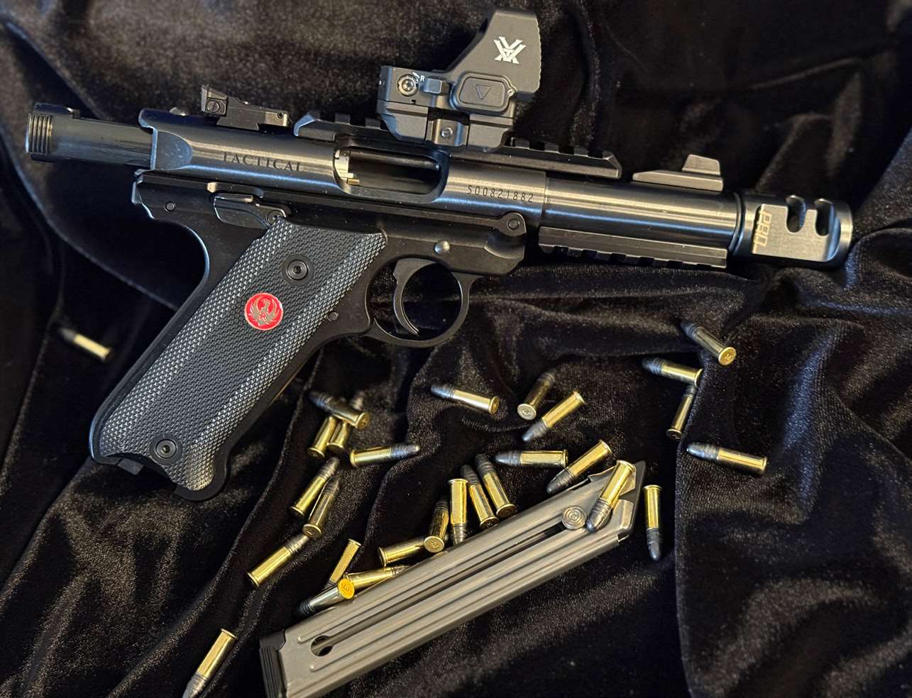 Ruger Mark IV Tactical pistol with Vortex Defender-XL red dot and Tandemkross compensator, surrounded by loose .22 LR rounds on a black satin background