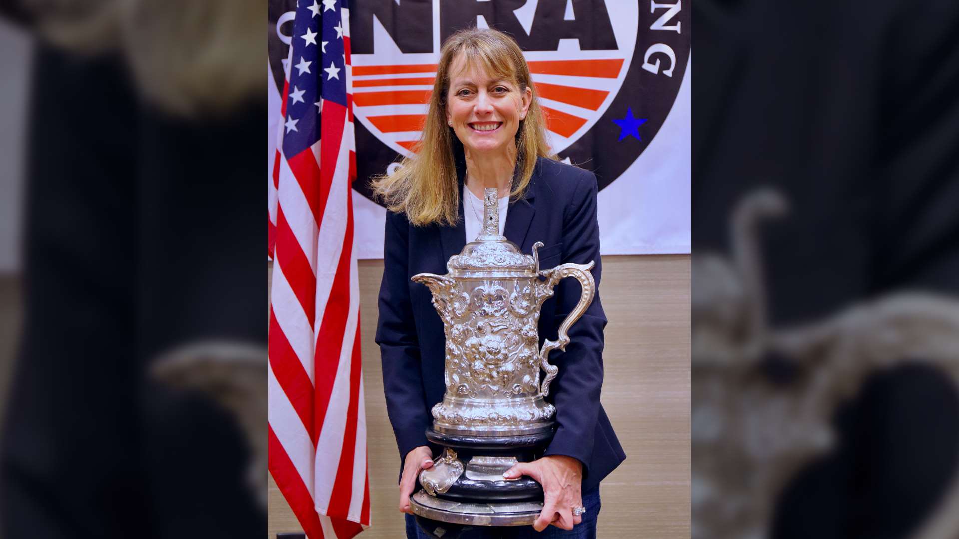 Kim Rowe smiles while holding the Leech Cup, an ornate silver trophy, at the 2026 NRA Long Range Awards ceremony