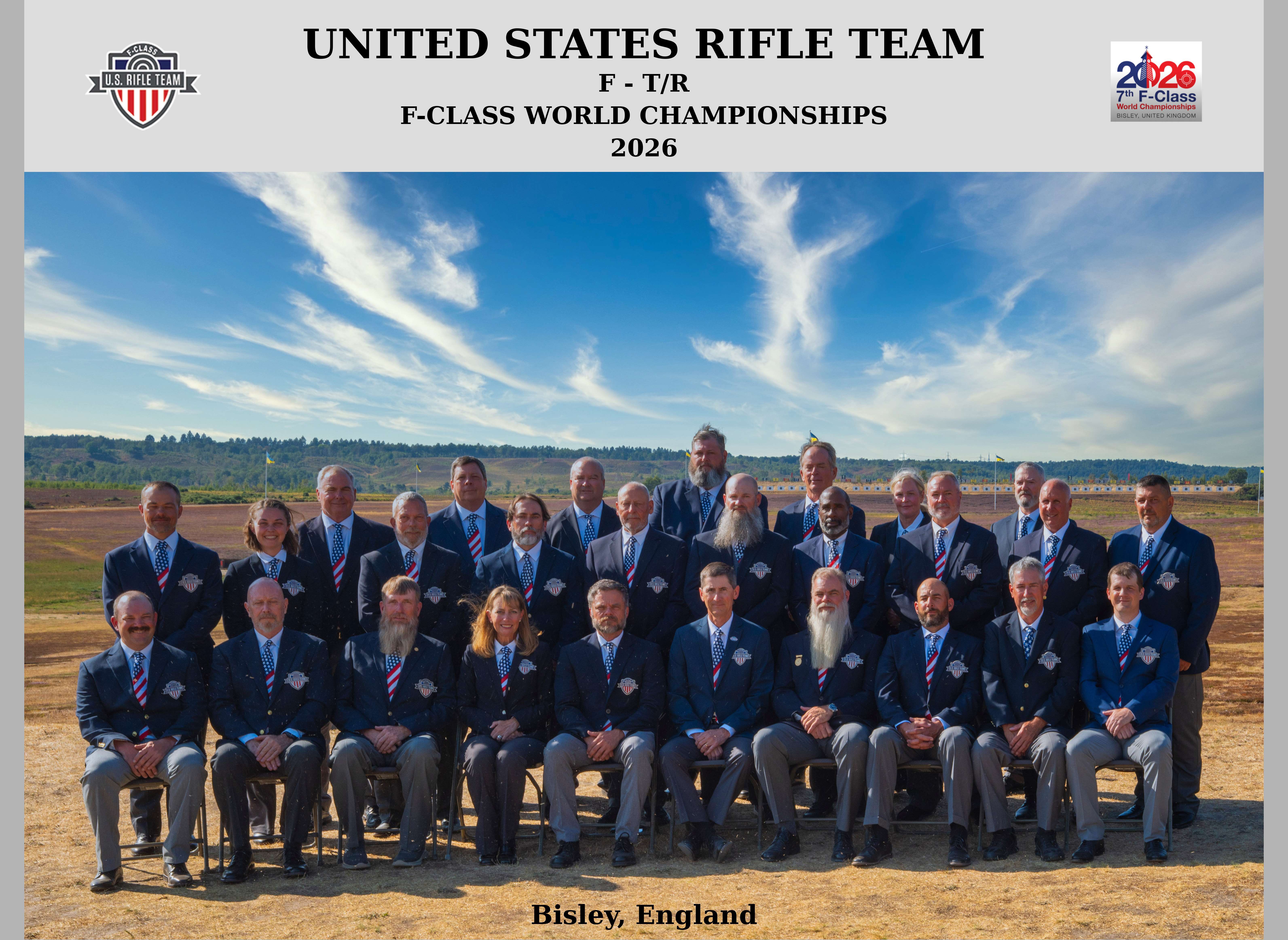 Official portrait of the 2026 United States F-T/R rifle team in navy blazers and striped ties, seated and standing in three rows on the range at Bisley with target butts and a blue sky behind them