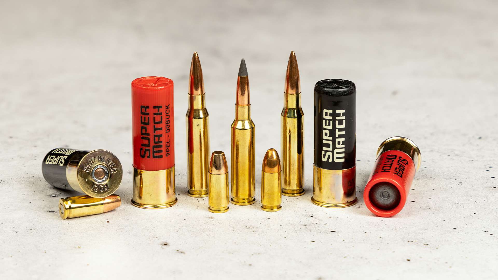 Winchester Super Match cartridge lineup showing 12-gauge shells, rifle cartridges and pistol rounds standing on concrete