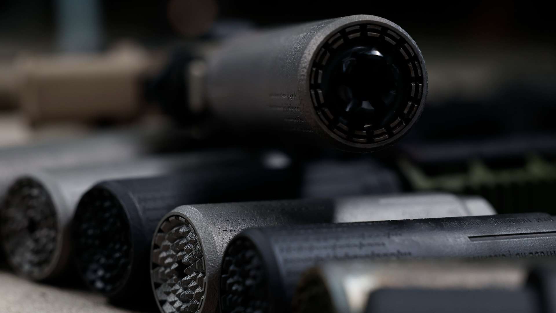 Several Polite Society Industries suppressors arranged muzzle-forward on a dark surface, showing different endcap and baffle patterns