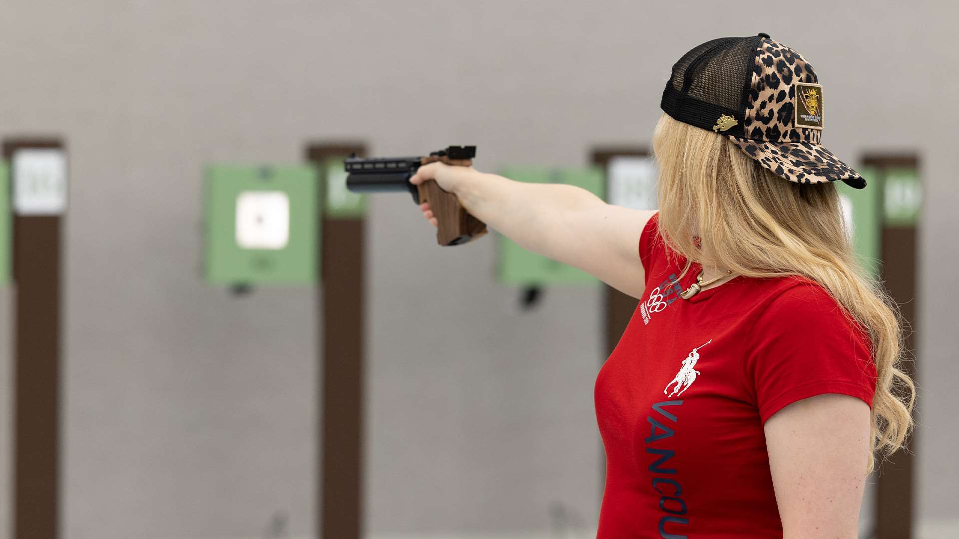 Pistol shooter aims downrange at USA Shooting and Hillsdale branded benches on the firing line inside the Nimrod Complex