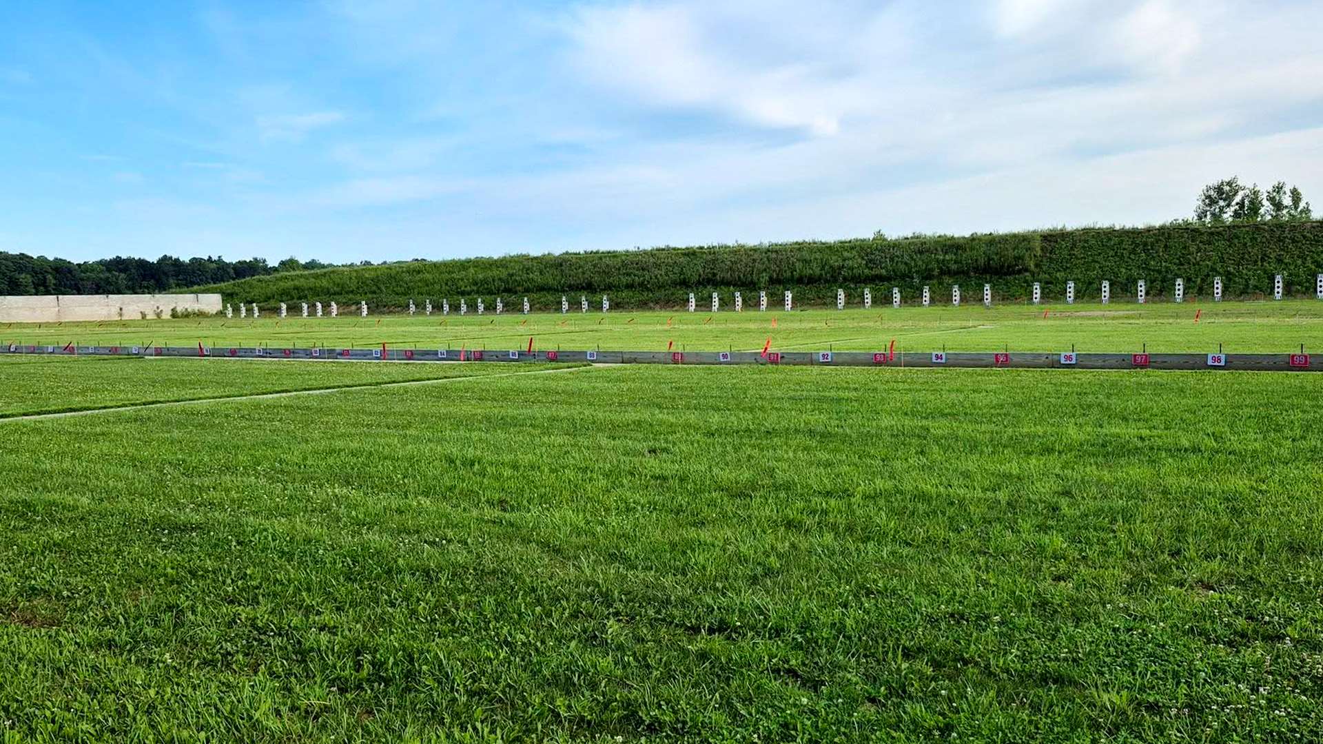 A wide, empty smallbore range at the Cardinal Shooting Center, with numbered firing points running across the foreground and a long row of target frames set against a grass berm under a blue sky