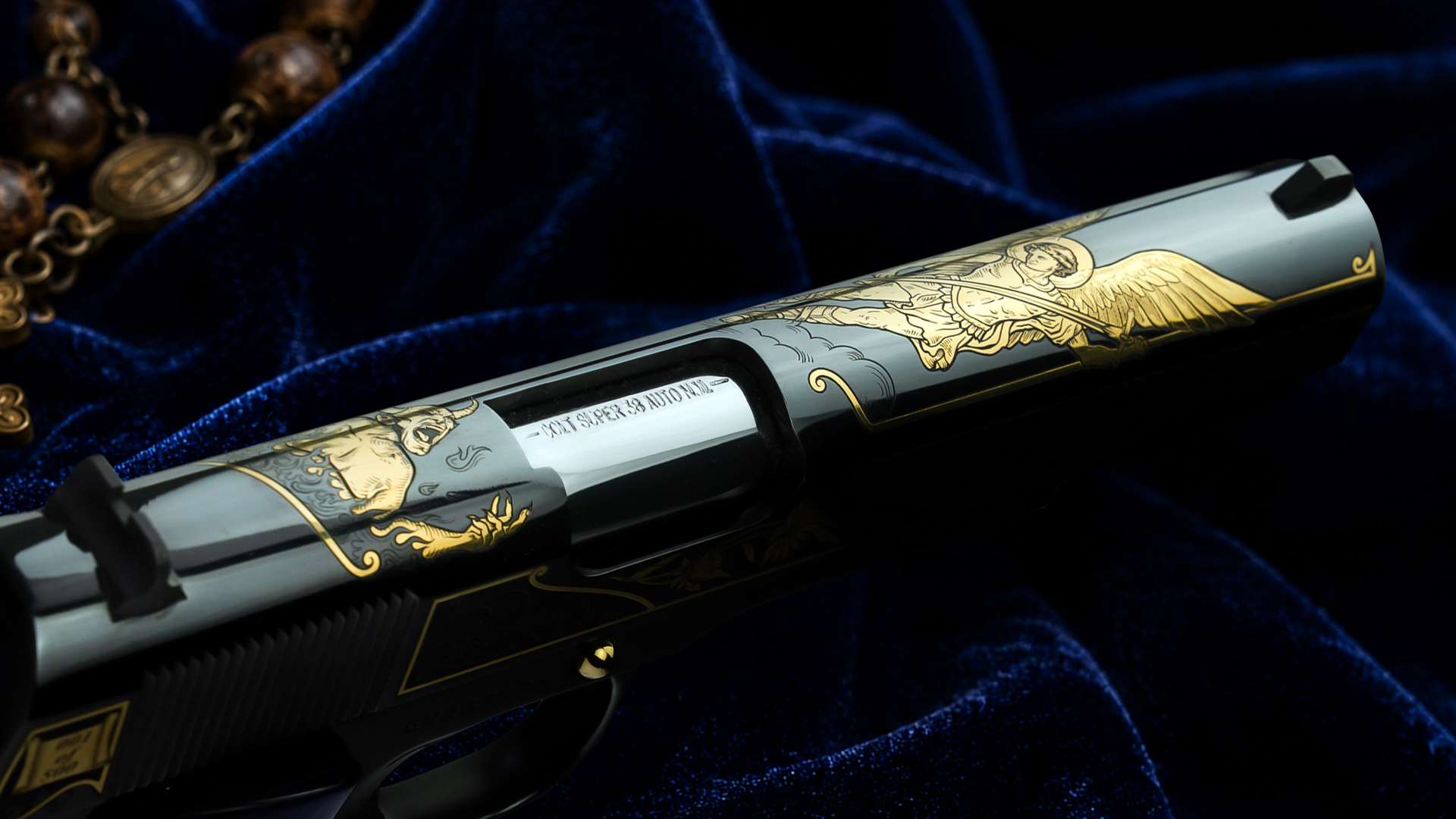 Close-up detail photograph of the top slide of the SK Customs San Miguel Arcángel Colt 1911 pistol, showing the 24-karat gold engraving of Saint Michael the Archangel battling Satan, photographed on blue velvet fabric