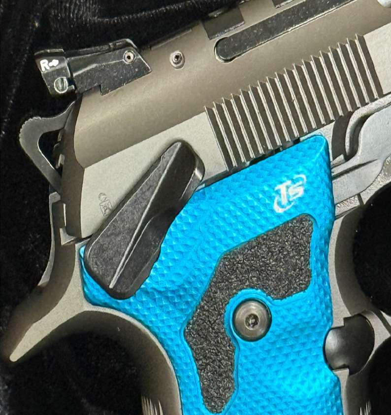 Macro detail of the Beretta 92X Performance Dark Series grip area, featuring oversized ambidextrous safety lever and blue checkered Toni aluminum grip panel
