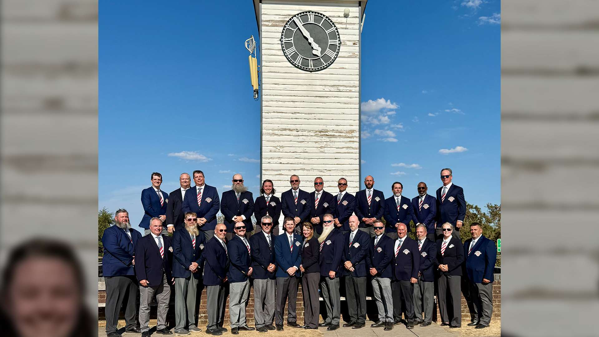 The United States F-T/R rifle team in navy blazers and striped ties, arranged in two rows at the base of the white clock tower at Bisley