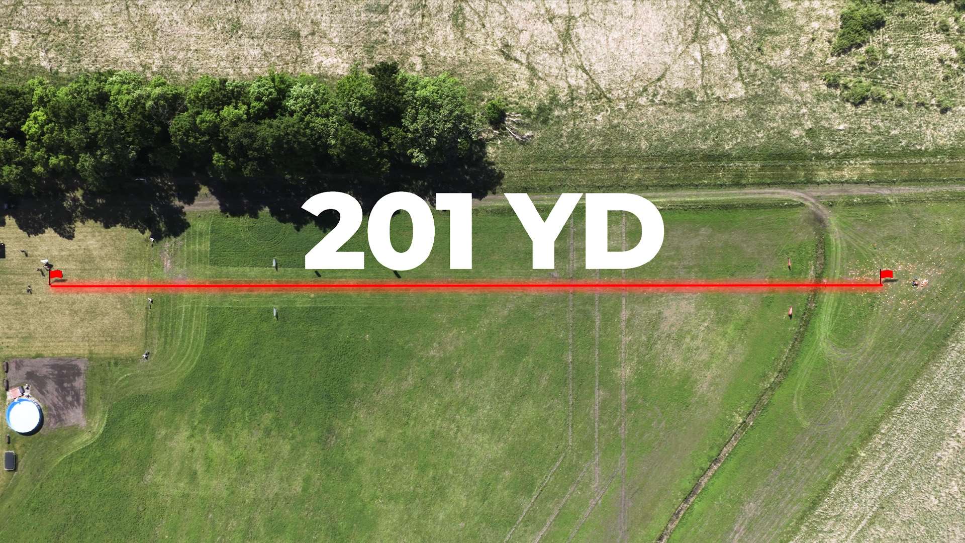 Aerial drone view of a grass field with a red line and flags marking the 201-yard distance of Steve Gould's record clay target shot, labeled 201 YD