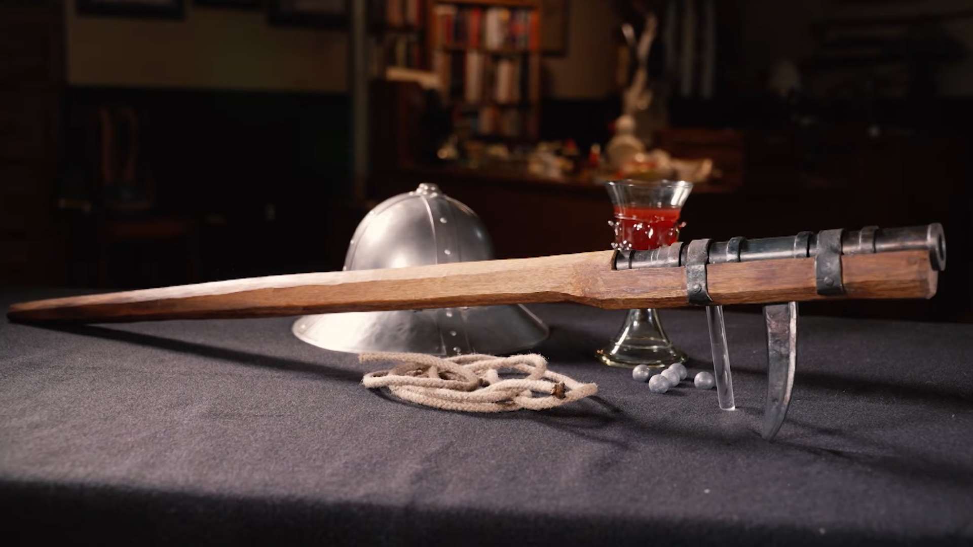 Full-length side view of a historic hand cannon on a table showing metal barrel and wooden tiller from American Rifleman TV I Have This Old Gun segment