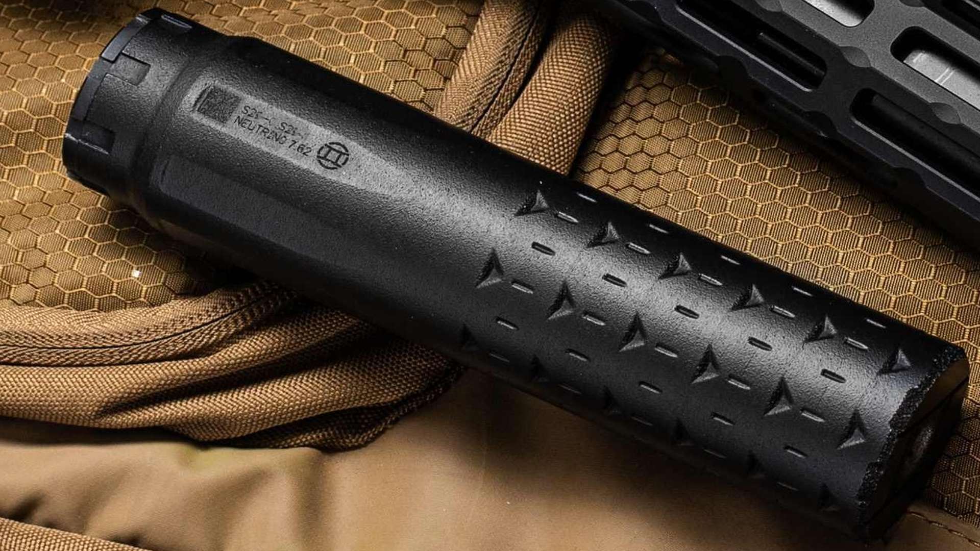 Close-up of Gemtech Neutrino 7.62 suppressor resting on a coyote brown rifle bag next to an M-Lok fore-end