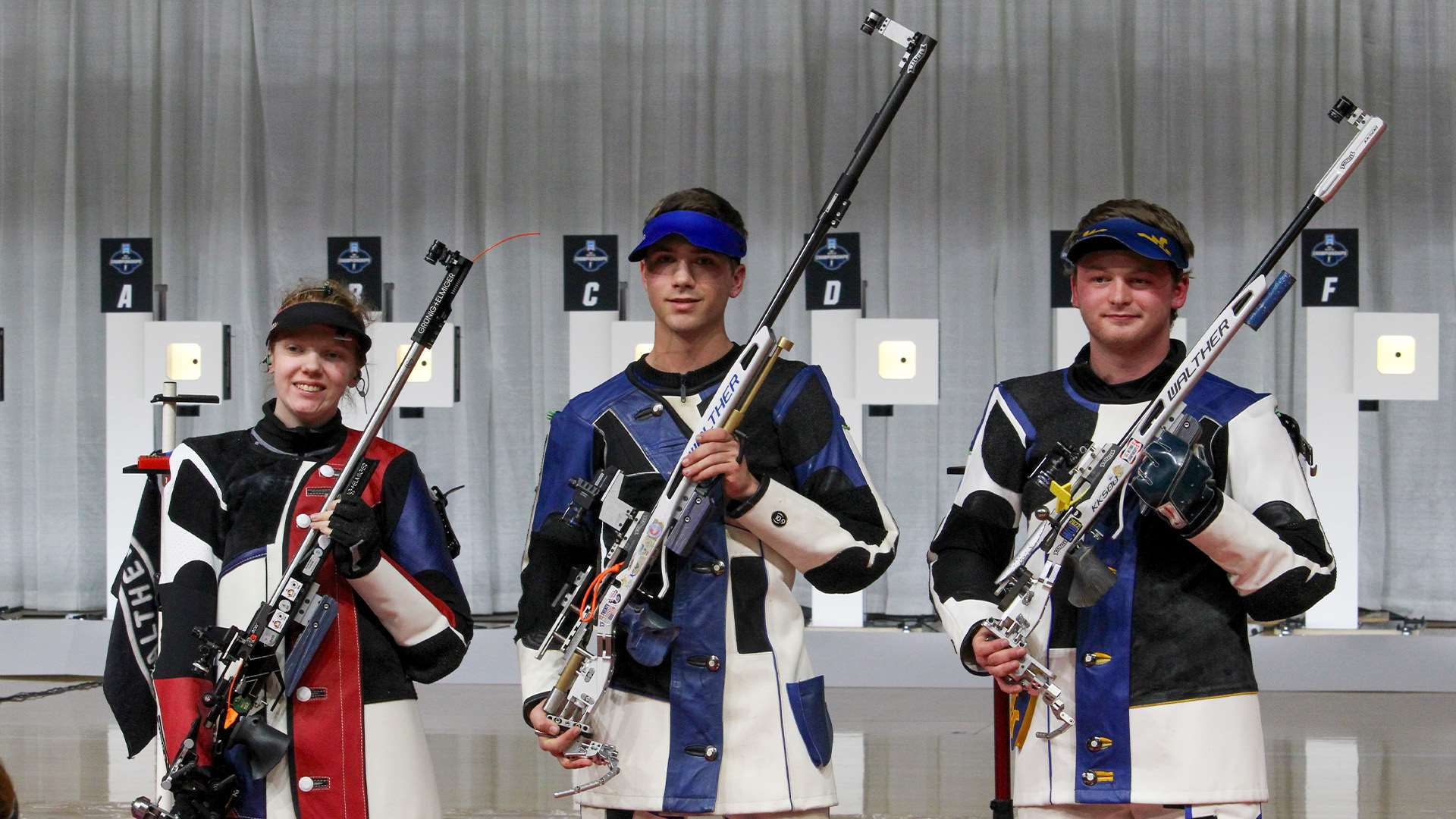 Three college rifle shooters in shooting jackets hold smallbore rifles upright after the smallbore final at the 2026 NCAA Rifle Championship