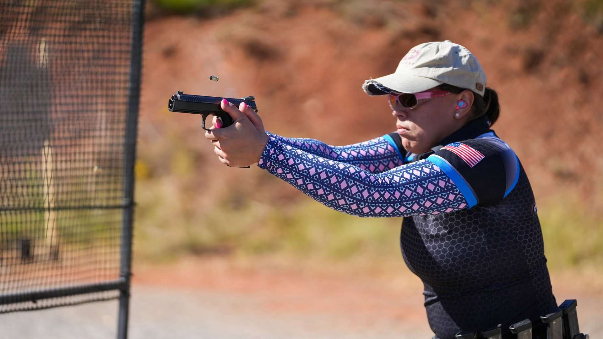 A Production Division competitor fires an iron-sighted pistol at USPSA Nationals, with spent brass ejecting mid-air.