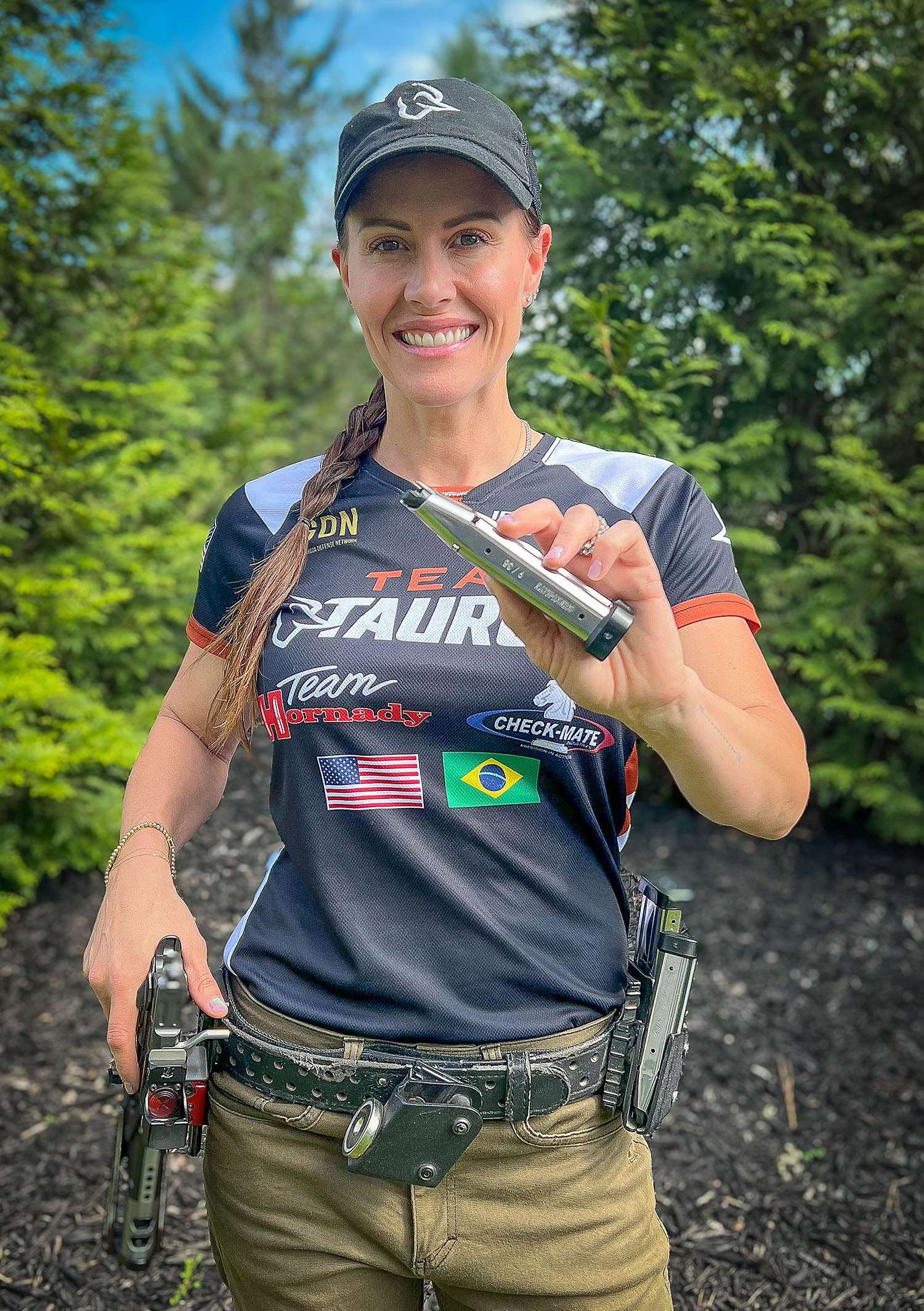 Jessie Harrison in a Team Taurus competition jersey, holding a Check-Mate pistol magazine, with a loaded belt rig and pistol at her side