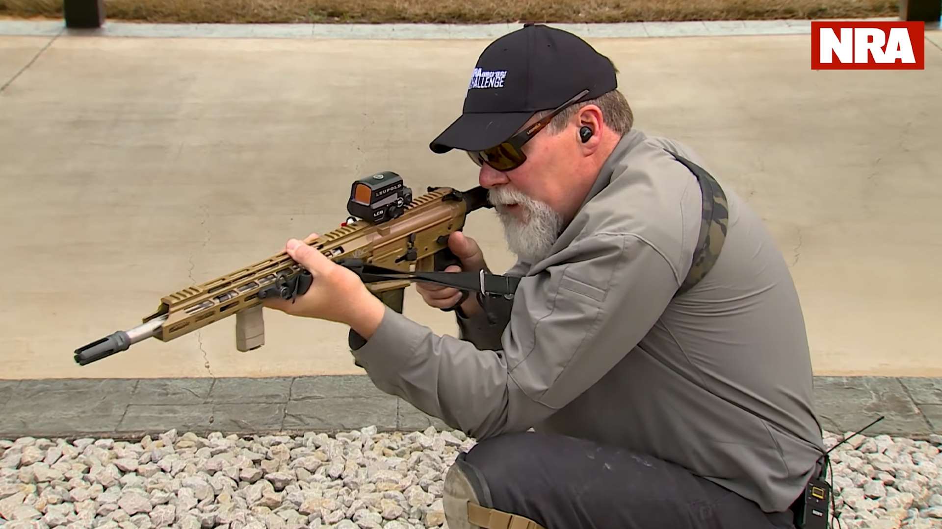 Kyle Lamb demonstrating kneeling position sling technique with elbow inside knee and arm rotated for stability during NRA America’s Rifle Challenge video